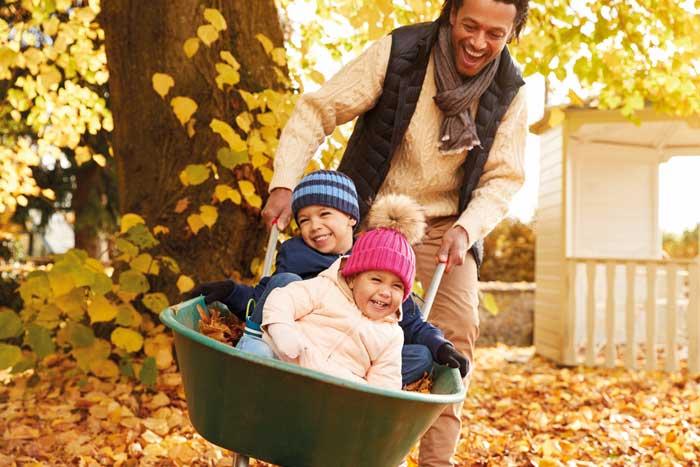 Dad with boy and girl in wheelbarrow, with an autumn background